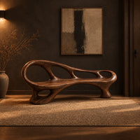 Long wooden bench with oval cutouts along the back rail and a flowing frame in a dark entryway at golden hour