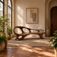 Long wooden bench with oval cutouts along the back rail and a flowing frame in a bright entryway with arched windows and plants