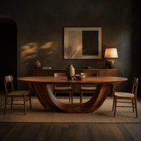 Oval dining table on a U shaped sculpted pedestal base in a dark dining room at golden hour