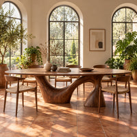 Oval dining table on a sweeping arm base and a tall cone column in a bright dining room with arched windows and plants