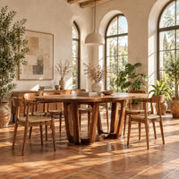 Oval dining table with sculpted arched legs joined by a low floor loop in a bright dining room with arched windows and plants