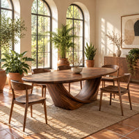 Oval dining table on a sculpted crescent base in a bright dining room with arched windows and plants
