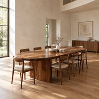 Oval dining table with a thick edge and two broad slab legs in a bright open plan dining room