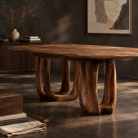 Corner detail of oval dining table on two pedestal bases with tall arched openings beside wood, brass and linen samples
