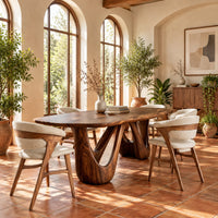 Oval dining table with two sculpted arch pedestals in a bright dining room with arched windows and plants
