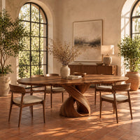 Oval dining table with a twisting ribbon pedestal and a hollow center in a bright dining room with arched windows and plants