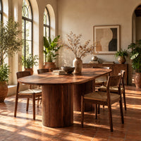 Oval dining table with two fluted cylinder bases in a bright dining room with arched windows and plants