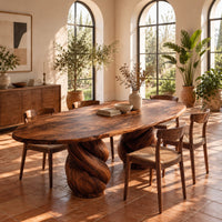 Oval dining table with two twisted rope pedestal bases in a bright dining room with arched windows and plants