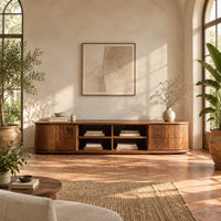 Oval ended tv stand with four open cubbies between two end cabinets in a bright living room with arched windows and plants