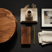 Corner detail of oval porthole coffee table with a low shelf beside wood, brass and linen samples