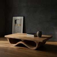 Pale hardwood coffee table with an undulating base in a dark studio against a charcoal wall
