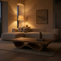 Pale hardwood coffee table with an undulating base in an evening room lit by two lamps