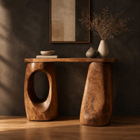 Console table with two chunky pebble shaped legs and a slim oval ended top in a dark studio against a charcoal plaster wall