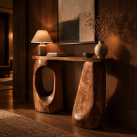 Console table with two chunky pebble shaped legs and a slim oval ended top in an evening entryway with walnut wall paneling