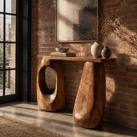 Console table with two chunky pebble shaped legs and a slim oval ended top in an industrial loft entryway with exposed brick