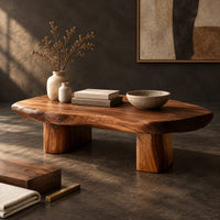Corner detail of pebble shaped coffee table with a smooth organic top and two thick column legs beside wood, brass and linen samples