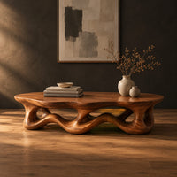 Low oval coffee table with a wavy base cut through by irregular openings in a dark studio against a charcoal plaster wall