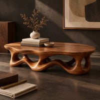 Corner detail of low oval coffee table with a wavy base cut through by irregular openings beside wood, brass and linen samples