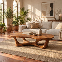 Pebble shaped coffee table on branching legs with open arches in a bright living room with arched windows and plants