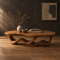 Pebble shaped coffee table with a rippling open ribbon base in a dark studio against a charcoal plaster wall