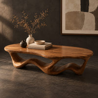 Corner detail of pebble shaped coffee table with a rippling open ribbon base beside wood, brass and linen samples