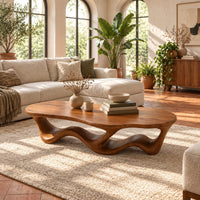 Pebble shaped coffee table with a rippling open ribbon base in a bright living room with arched windows and plants
