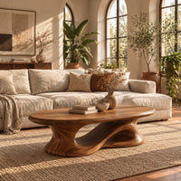 Oval coffee table on a heavy pedestal with a swirling hollow in a bright living room with arched windows and plants