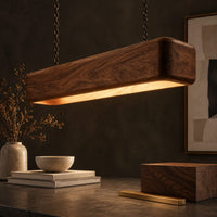 Corner detail of long wood beam pendant light with soft corners and a warm glow below beside wood, brass and linen samples