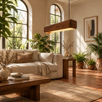 Long wood beam pendant light with soft corners and a warm glow below in a bright living room with arched windows and plants