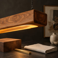 Corner detail of pendant light shaped as a long wood beam with a warm glowing underside beside wood, brass and linen samples