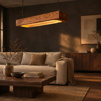 Pendant light shaped as a long wood beam with a warm glowing underside in a dark living room at golden hour
