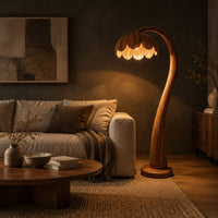 Floor lamp with a flower petal shade on a slender arching stem in a dark living room at golden hour