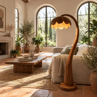 Floor lamp with a flower petal shade on a slender arching stem in a bright living room with arched windows and plants