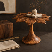 Corner detail of end table with a carved petal top on a flaring trumpet shaped pedestal beside wood, brass and linen samples
