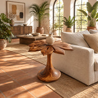 End table with a carved petal top on a flaring trumpet shaped pedestal in a bright living room with arched windows and plants