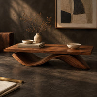 Corner detail of rectangular coffee table with a flat plank top on a single rolling wave base beside wood, brass and linen samples