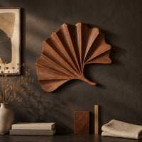 Detail of fan shaped leaf wall art with carved radiating ridges and a curled stem beside wood, brass and linen samples