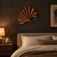 Fan shaped leaf wall art with carved radiating ridges and a curled stem above a bed in a dusk lit bedroom