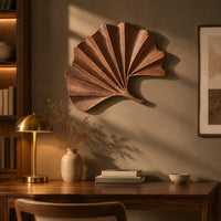 Fan shaped leaf wall art with carved radiating ridges and a curled stem above a desk in a dark study corner