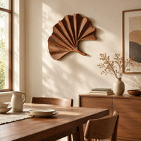 Fan shaped leaf wall art with carved radiating ridges and a curled stem beside a dining table in natural light
