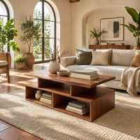Coffee table with a raised slab top over two open cubbies in a bright living room with arched windows and plants