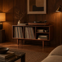Open record player stand with four bays on tapered legs in an evening living room with walnut wall paneling