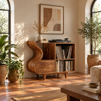Record player stand with a flowing wave side and two open cubbies in a bright living room with arched windows and plants