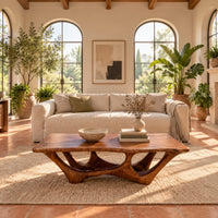Rectangular coffee table with a slab top and branching arched base in a bright living room with arched windows and plants