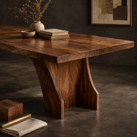 Corner detail of rectangular dining table with a thick slab top on a wide hourglass pedestal beside wood, brass and linen samples
