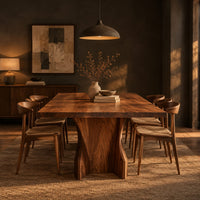 Rectangular dining table with a thick slab top on a wide hourglass pedestal in a dark dining room at golden hour