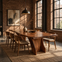 Rectangular dining table with a thick slab top on a wide hourglass pedestal in an industrial loft dining room with exposed brick