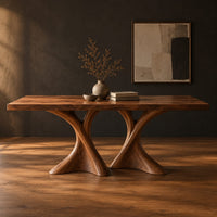 Rectangular dining table on two hourglass pedestal legs in a dark studio against a charcoal plaster wall