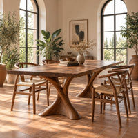 Rectangular dining table on two hourglass pedestal legs in a bright dining room with arched windows and plants