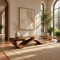 Low bench with a long slab seat on a flowing ribbon shaped base in a bright entryway with arched windows and plants